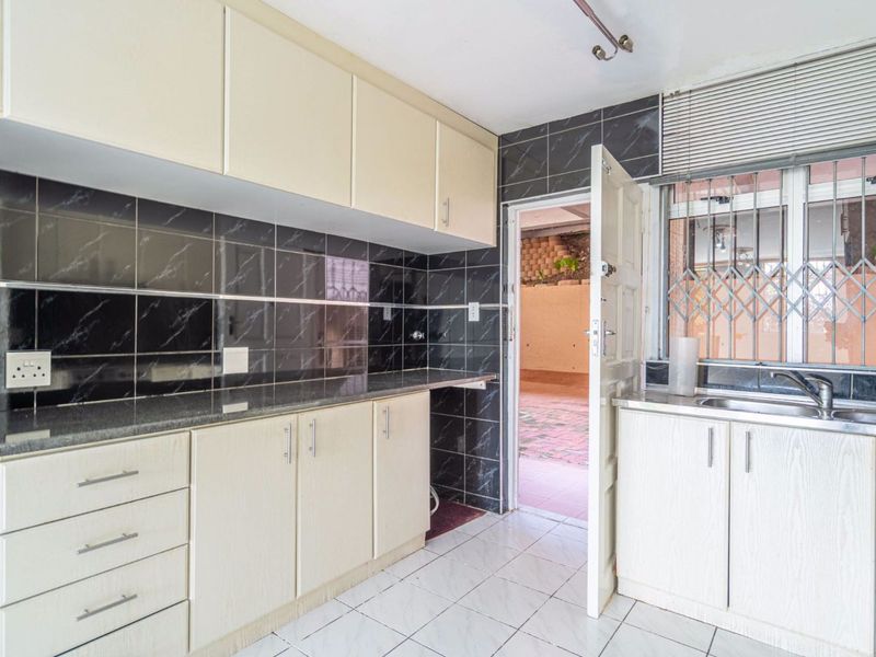 A functional kitchen featuring built-in cabinetry, granite countertops, a stainless steel sink, and dark tiled backsplash with direct access to an outdoor area.