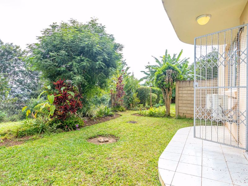 A private garden area featuring a tiled patio, security gate, and established landscaping, providing a functional outdoor space for the property.