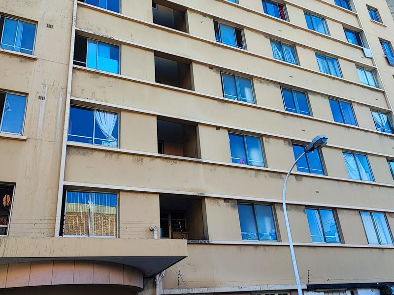 A multi-story apartment building facade featuring uniform window placement, concrete balcony recesses, and visible exterior weathering.