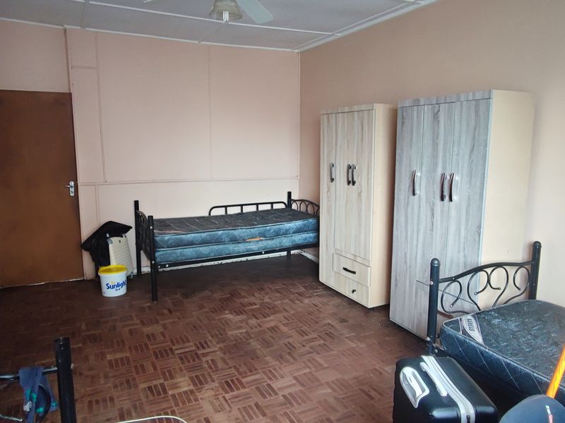 A bedroom featuring parquet flooring and a ceiling fan, offering a functional space with potential for cosmetic updates.