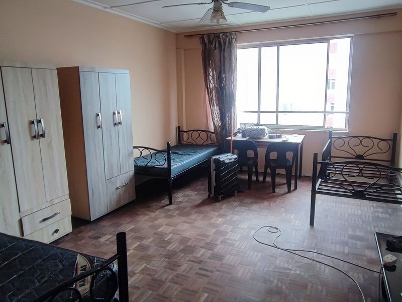 A spacious bedroom featuring parquet flooring, a ceiling fan, and large windows providing natural light.
