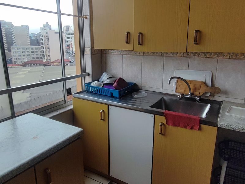 A compact kitchen featuring dated laminate cabinetry, a stainless steel sink, and a large window offering an urban city view.