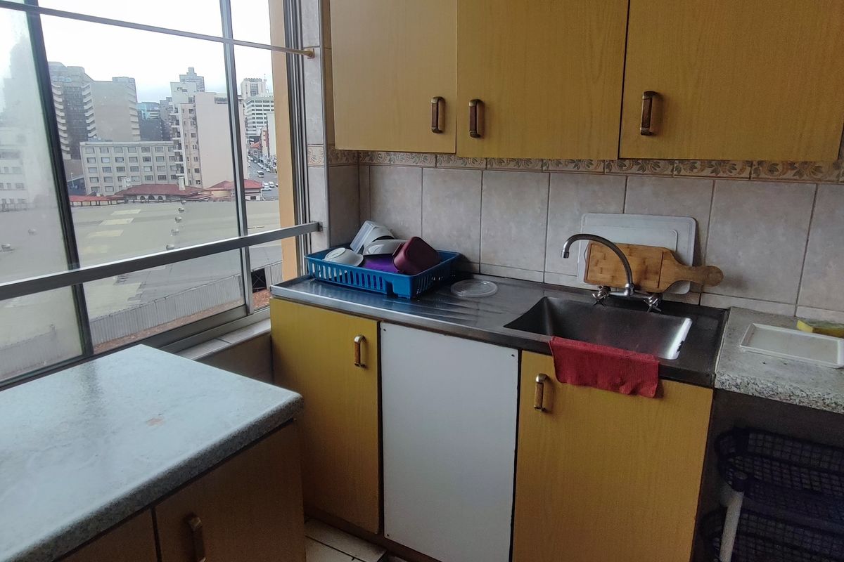 A compact kitchen featuring dated laminate cabinetry, a stainless steel sink, and a large window offering an urban city view.