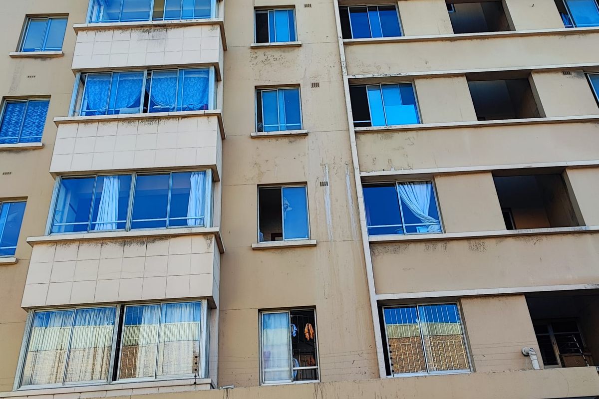 Front elevation of a multi-story apartment building featuring tiled facade sections and aluminium-framed windows showing signs of exterior weathering.