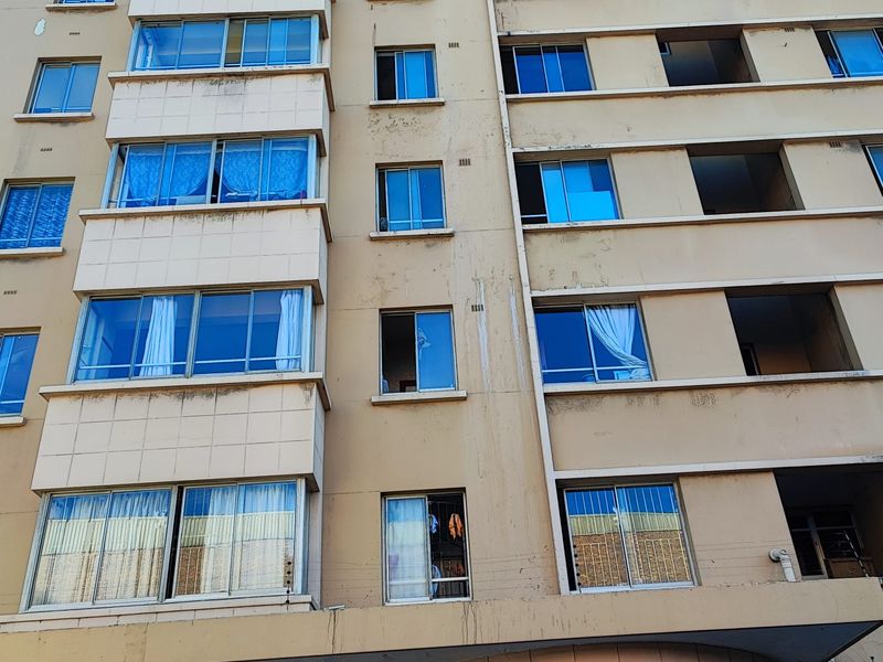Front elevation of a multi-story apartment building featuring tiled facade sections and aluminium-framed windows showing signs of exterior weathering.