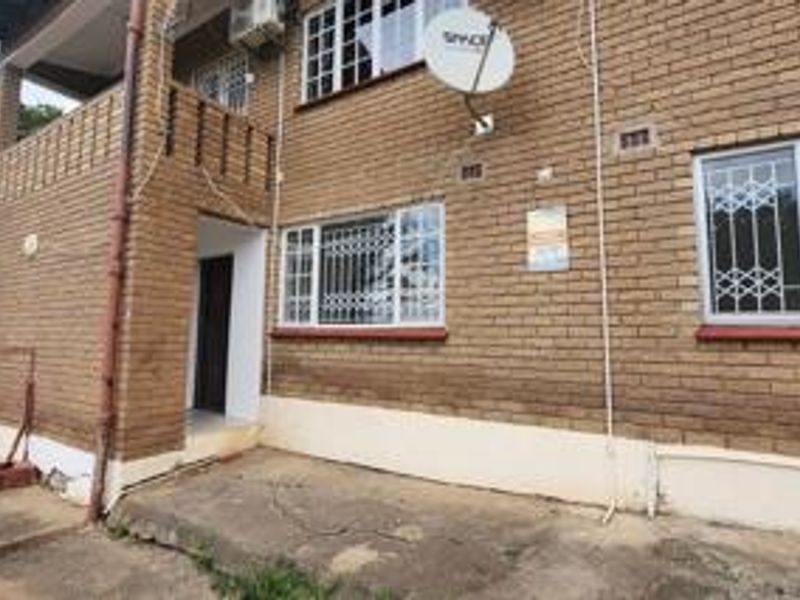Rear exterior view of a face brick residential building featuring security bars on windows, a concrete patio area, and an installed satellite dish.