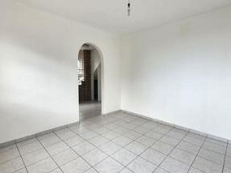An empty living room featuring neutral tiled flooring and a distinctive arched doorway leading to an adjacent space.