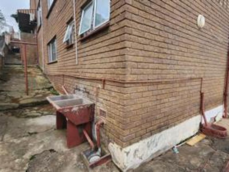 Rear exterior view of the property showing brick facade, concrete paving, and an external laundry sink area with visible signs of wear.