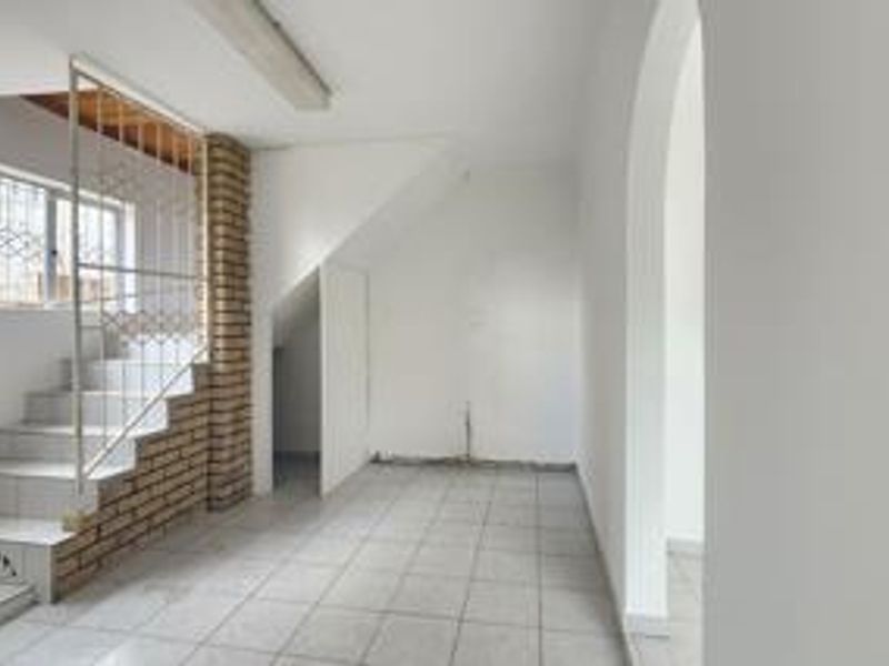An empty hallway featuring a tiled staircase with a brick accent wall, security gate, and an arched entryway leading to adjacent living spaces.