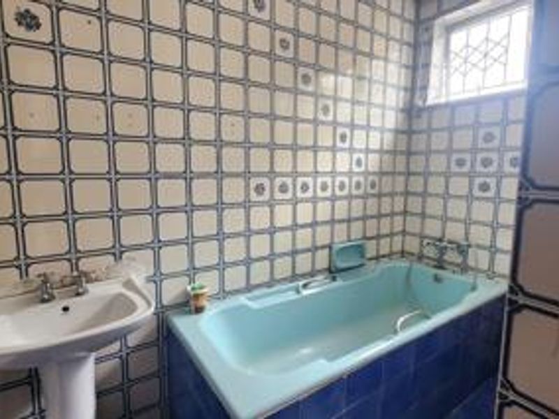 A dated bathroom featuring a pedestal basin and a built-in bathtub with extensive decorative wall tiling.