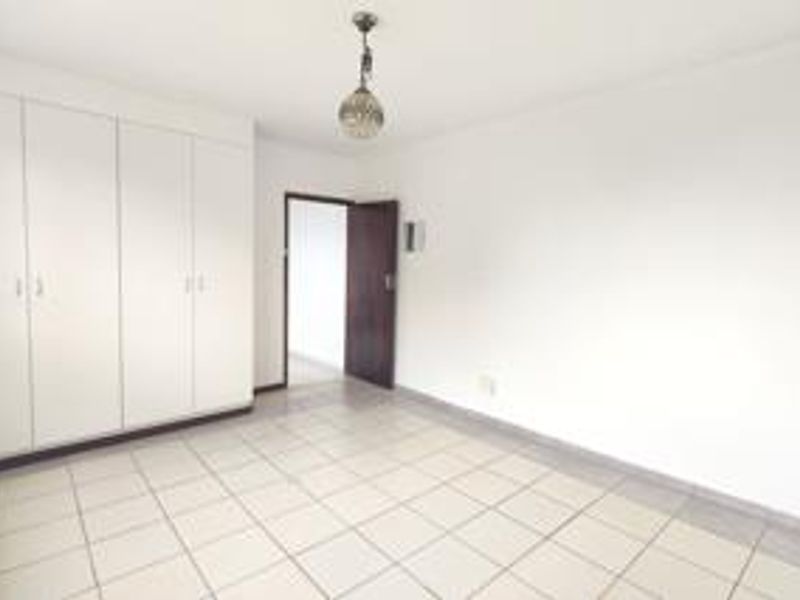 A bright, empty bedroom featuring neutral tiled flooring and ample built-in cupboard storage space.