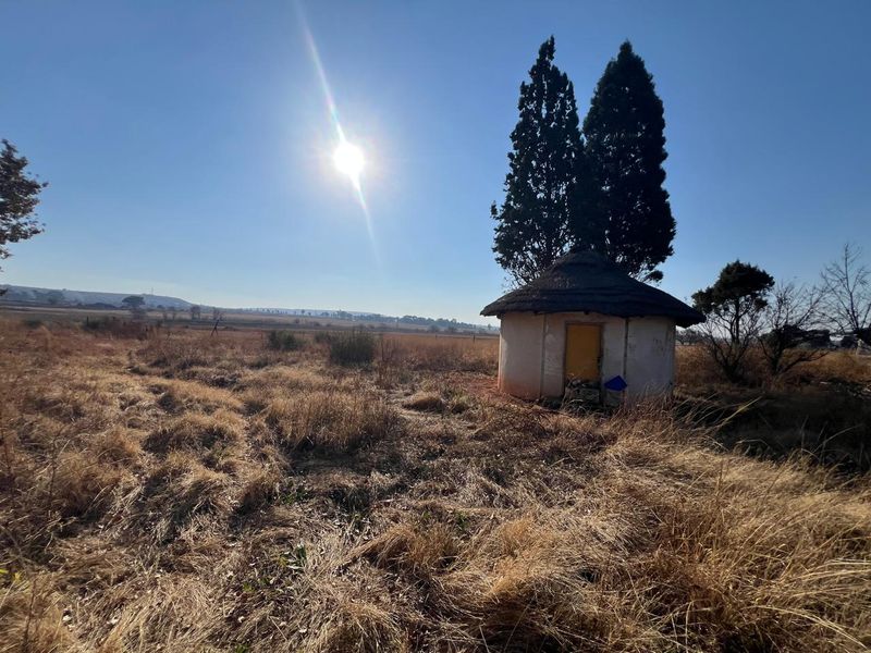 A small, circular thatched-roof structure situated in an open, dry field on a farm property.