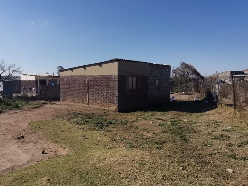 A view of the rear exterior of the property featuring brick construction and a corrugated metal roof set on an unpaved plot.