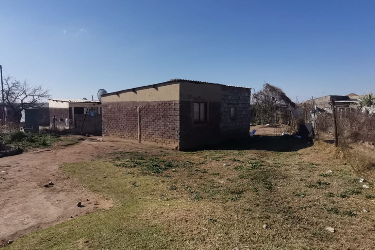 A view of the rear exterior of the property featuring brick construction and a corrugated metal roof set on an unpaved plot.