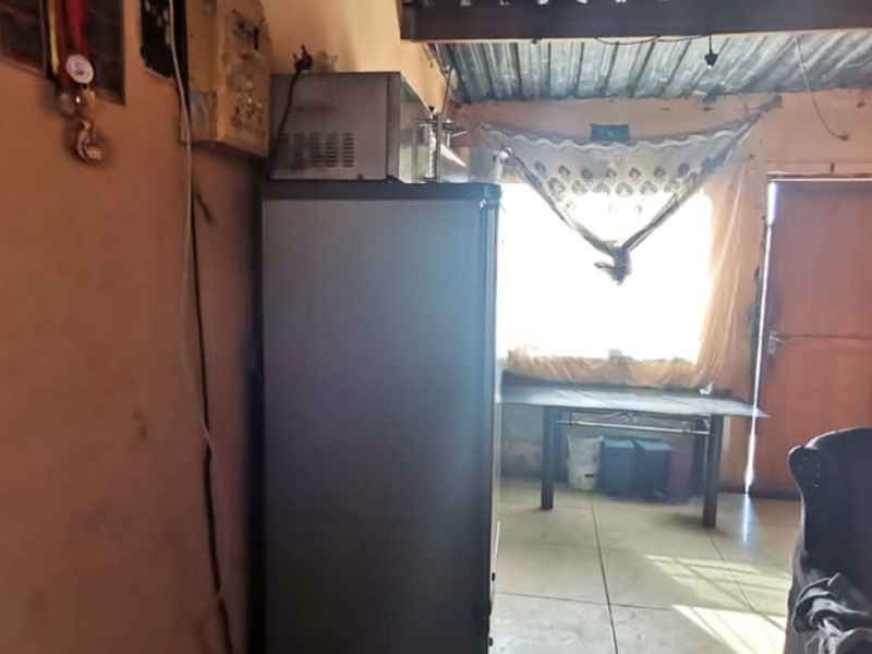 A living area featuring tiled flooring and an exposed corrugated metal ceiling, requiring significant cosmetic updates and maintenance to improve the overall condition.
