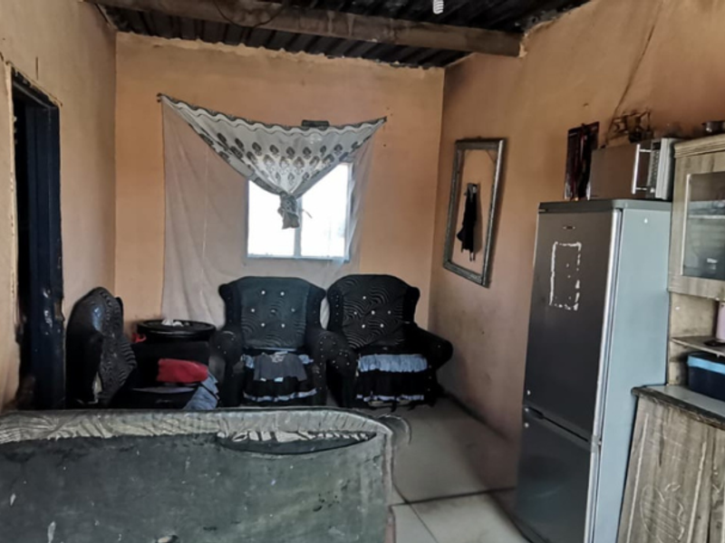 Open plan living area featuring tiled flooring and exposed ceiling beams, requiring significant cosmetic renovation and wall repairs.