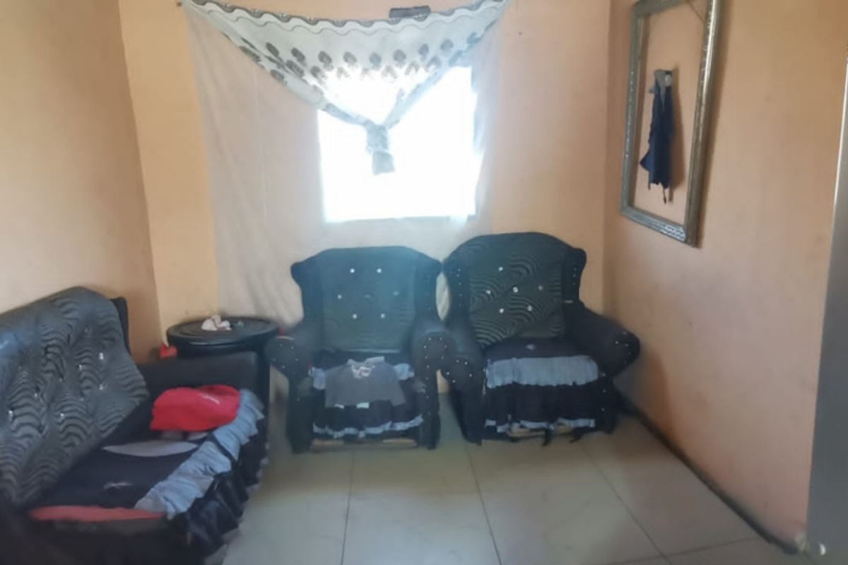 A living room area featuring tiled flooring and a window, currently showing signs of wear on the wall surfaces.