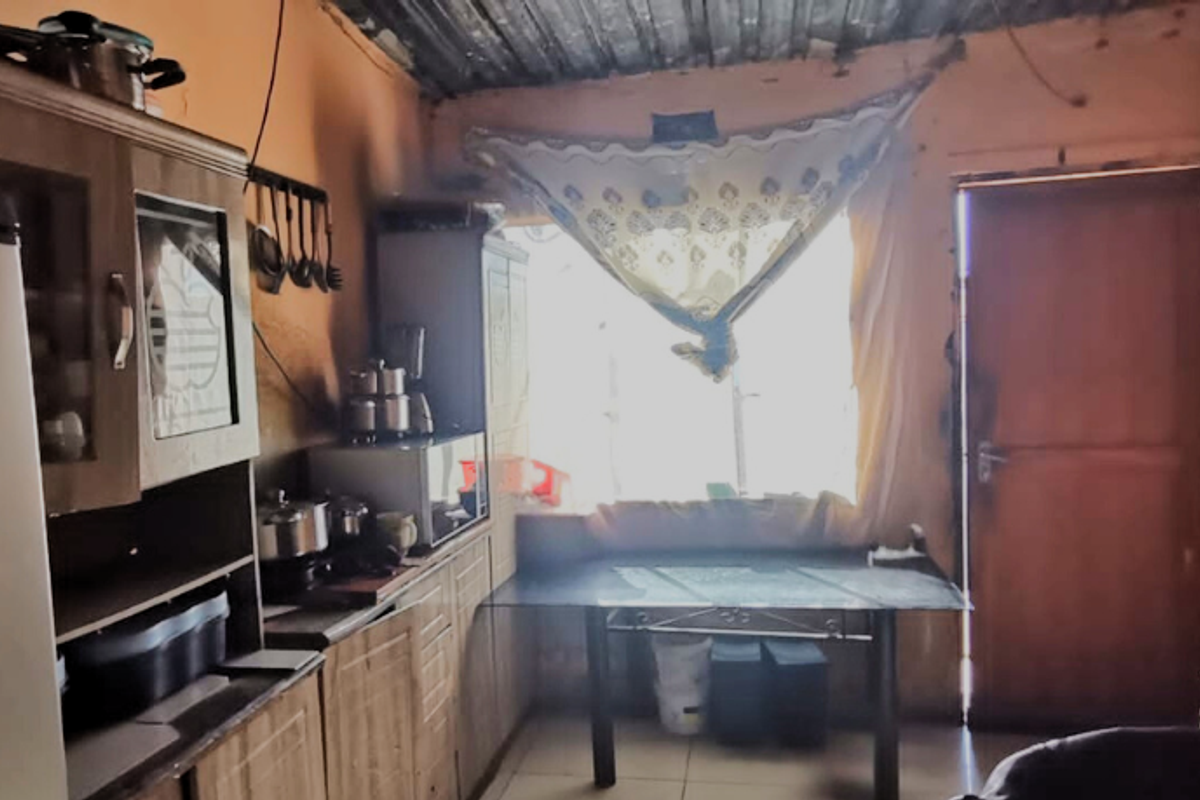 A dated kitchen area featuring built-in cabinetry, tiled floors, and a corrugated metal ceiling, requiring significant cosmetic updates and maintenance.