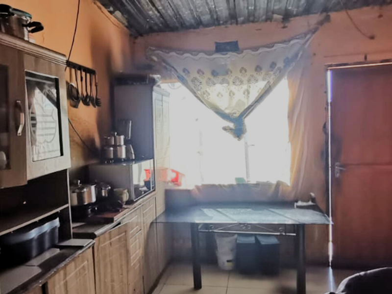 A dated kitchen area featuring built-in cabinetry, tiled floors, and a corrugated metal ceiling, requiring significant cosmetic updates and maintenance.