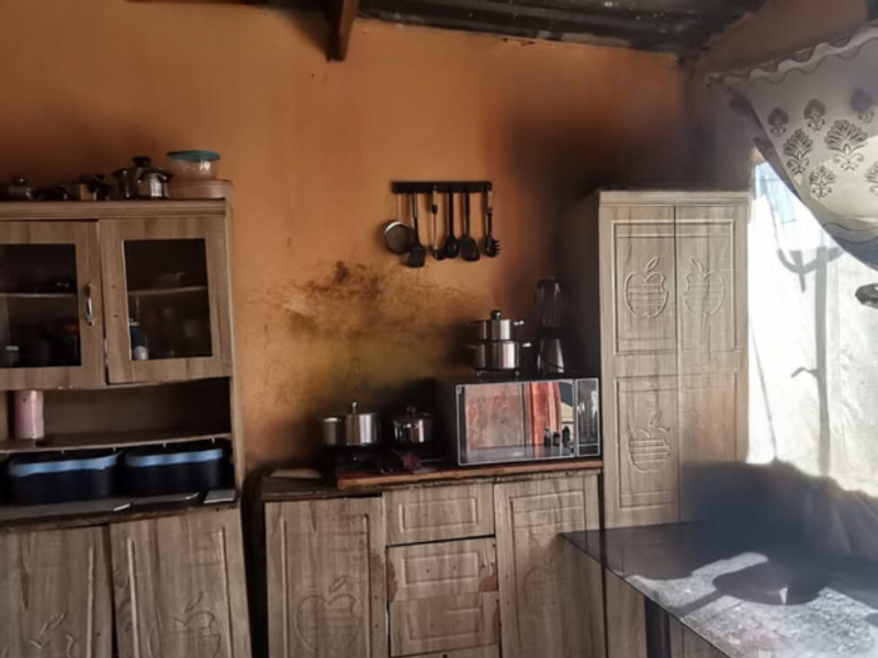 A dated kitchen area featuring built-in wooden cabinetry and counter space, requiring significant cosmetic updates and wall repairs to improve the overall condition.