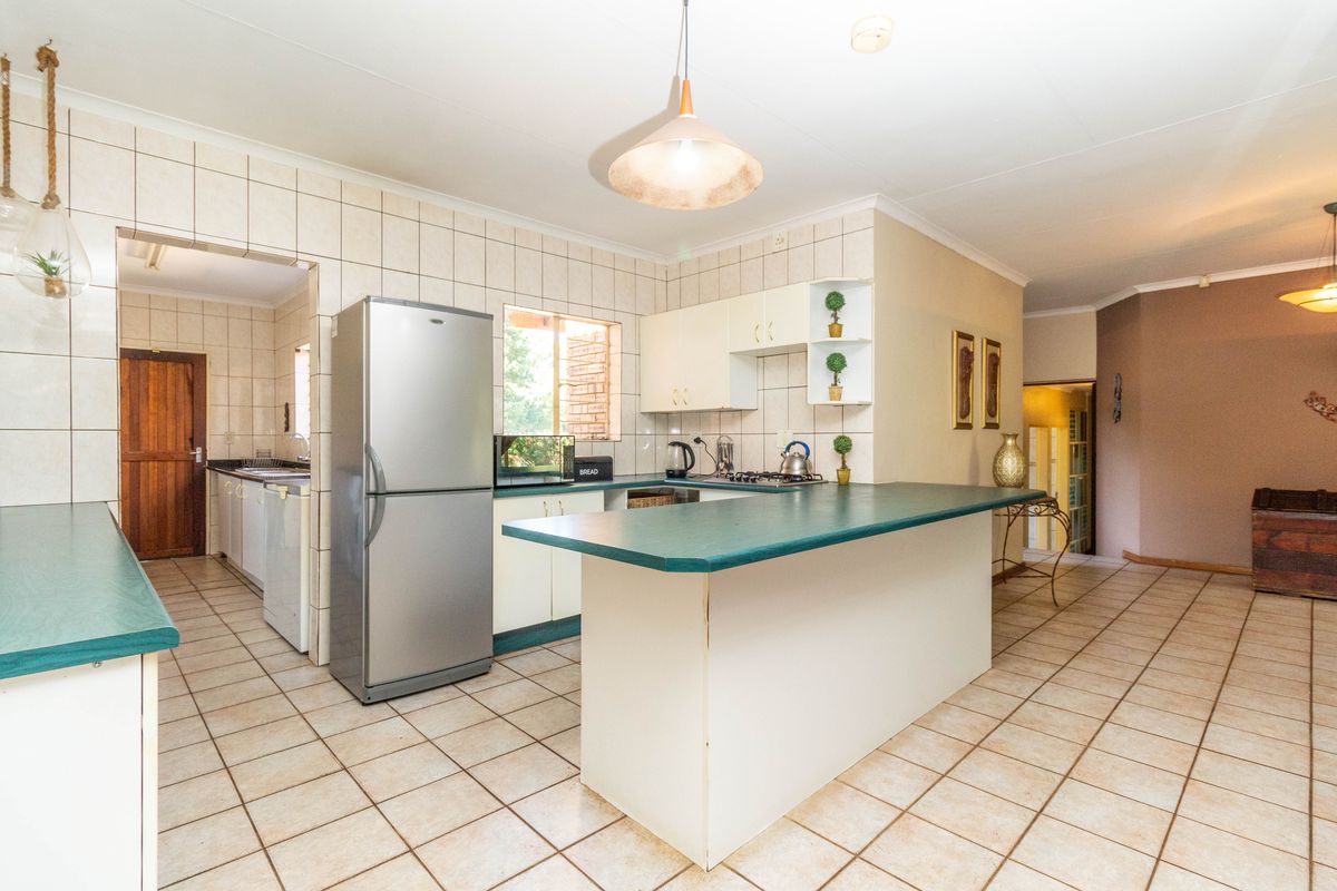 A functional kitchen featuring a breakfast bar, tiled flooring, and a separate scullery area, offering a practical layout for daily meal preparation.