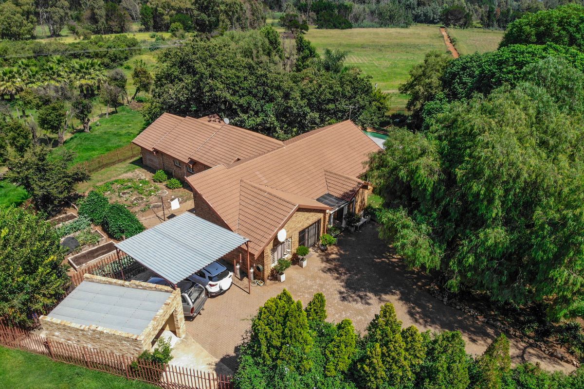 Aerial view of a residential property featuring a tiled roof, paved driveway, carport, and expansive surrounding garden and rural landscape.