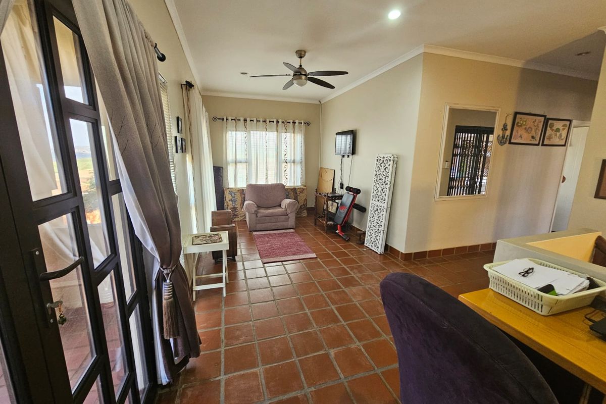 A spacious living area featuring terracotta floor tiles, recessed ceiling lighting, a ceiling fan, and large glass doors leading to an outdoor space.