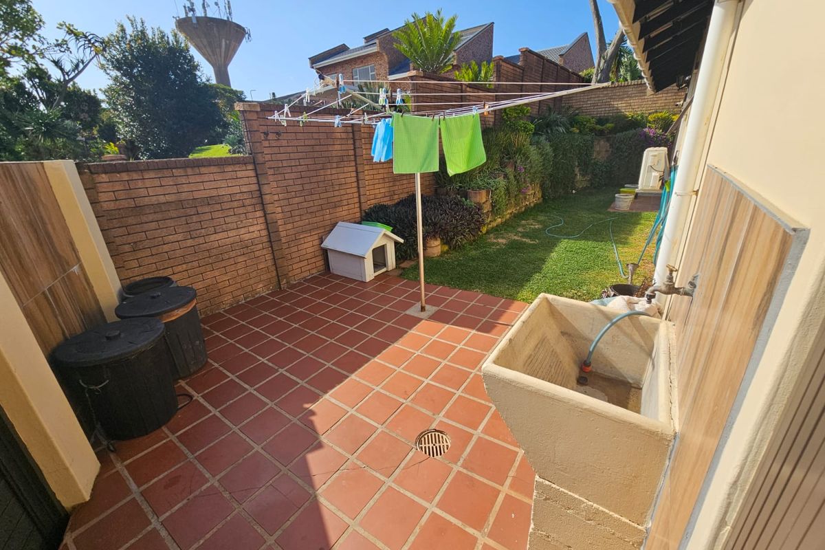 A functional rear courtyard featuring terracotta tiled flooring, a built-in utility sink, and direct access to a private garden area.