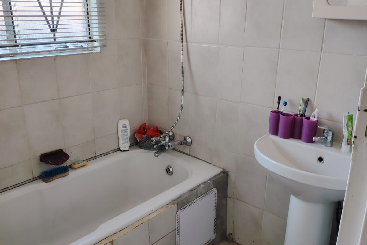 Compact bathroom featuring a bathtub with shower mixer, pedestal basin, and tiled finishes. The space would benefit from cosmetic updates and grout maintenance.