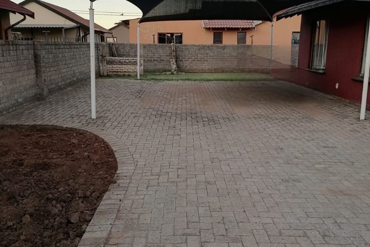 Rear exterior area featuring a paved driveway with a shade sail carport and perimeter brick walling.