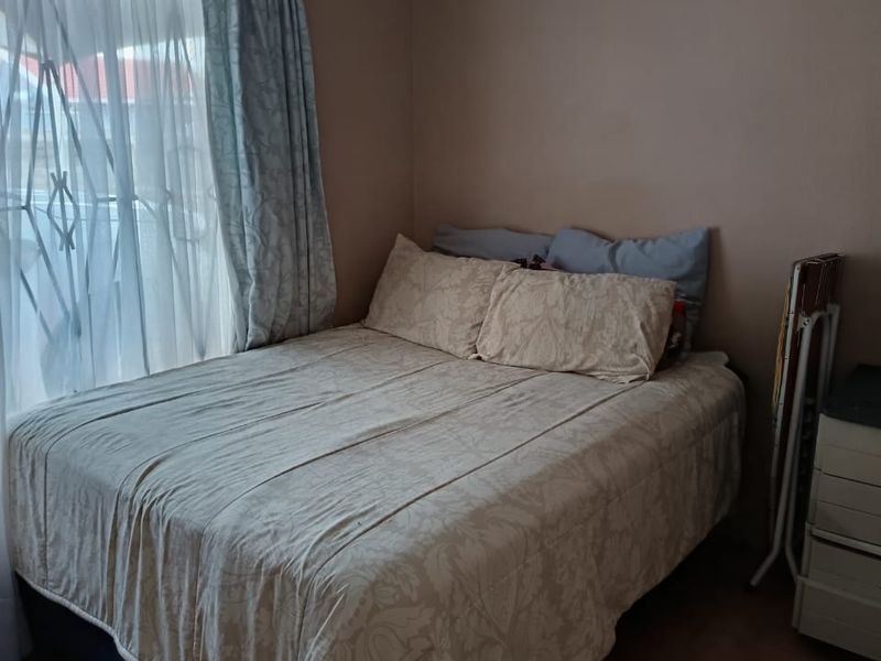 A standard bedroom featuring a window with a security gate and curtain rail, providing a functional space for rest.