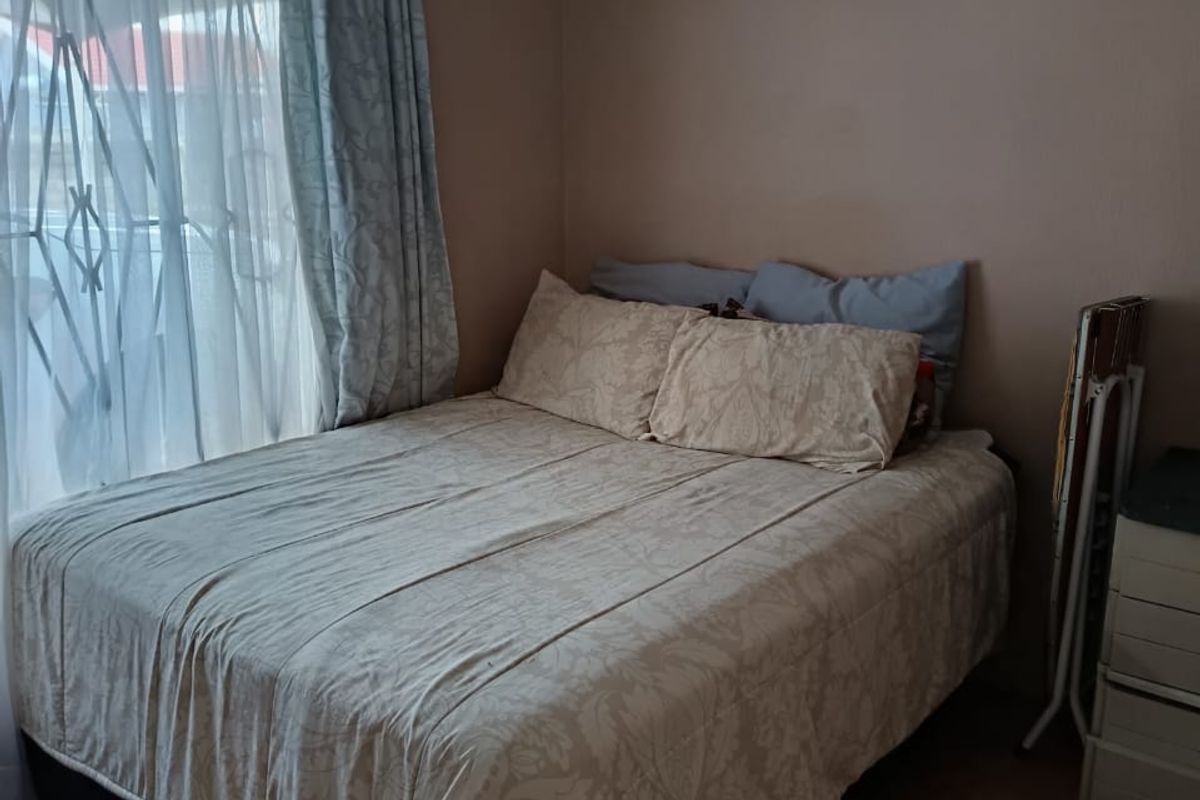 A standard bedroom featuring a window with a security gate and curtain rail, providing a functional space for rest.