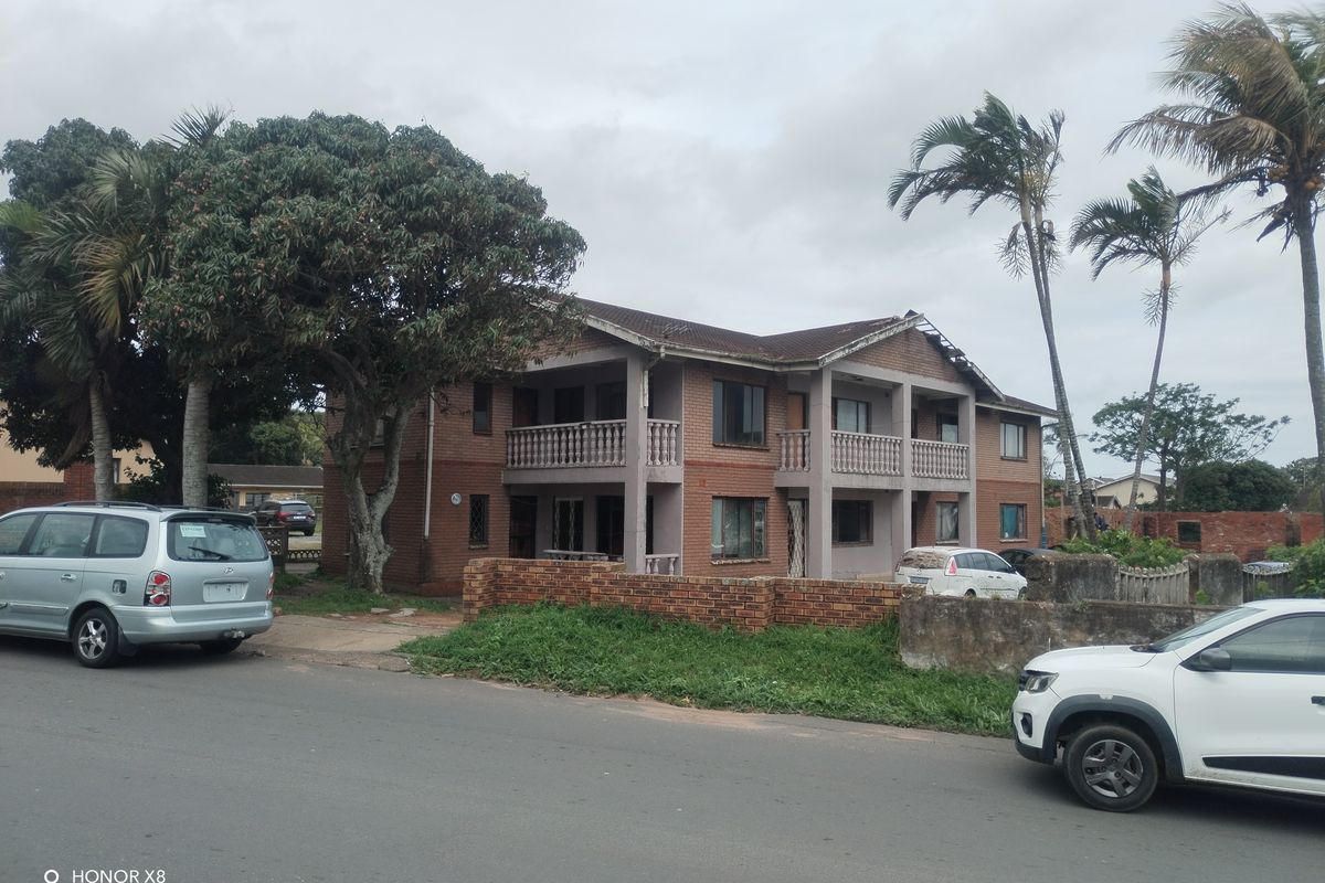 Two-story brick residential building featuring upper-level balconies with concrete balustrades, situated on a corner lot with a perimeter brick boundary wall.