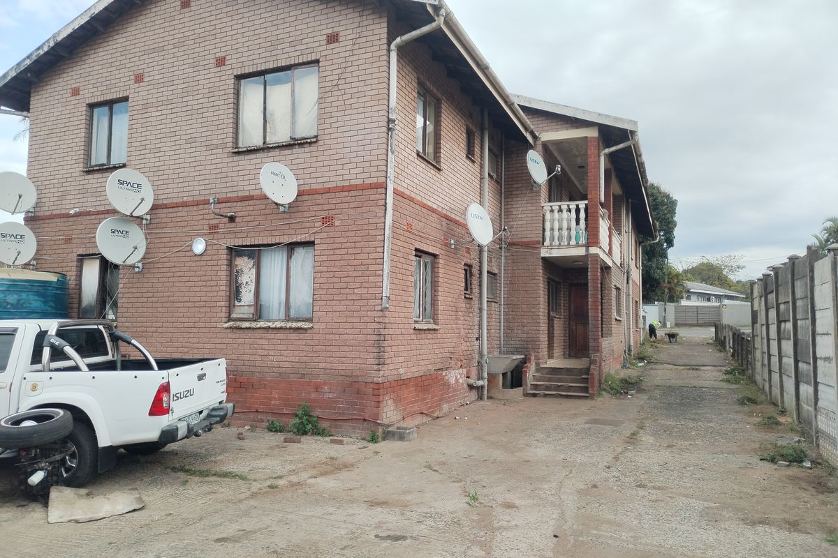 Rear view of a multi-story face brick residential building featuring a concrete driveway, balcony, and perimeter boundary walling.