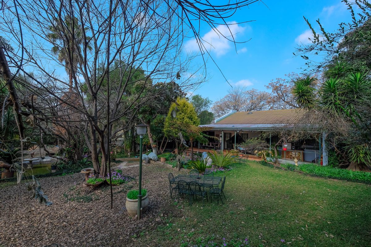 A spacious rear garden featuring a covered patio area, mature trees, and established landscaping, providing a private outdoor space for relaxation.