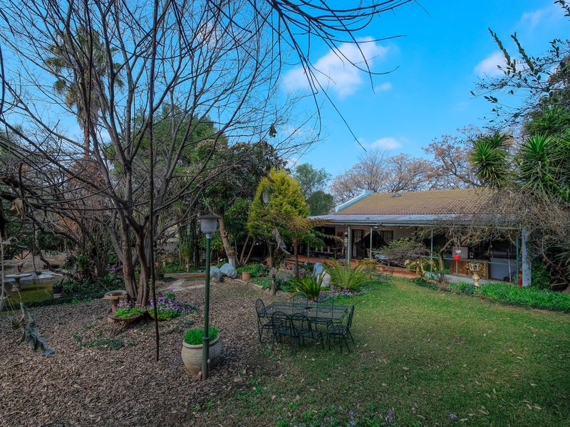 A spacious rear garden featuring a covered patio area, mature trees, and established landscaping, providing a private outdoor space for relaxation.