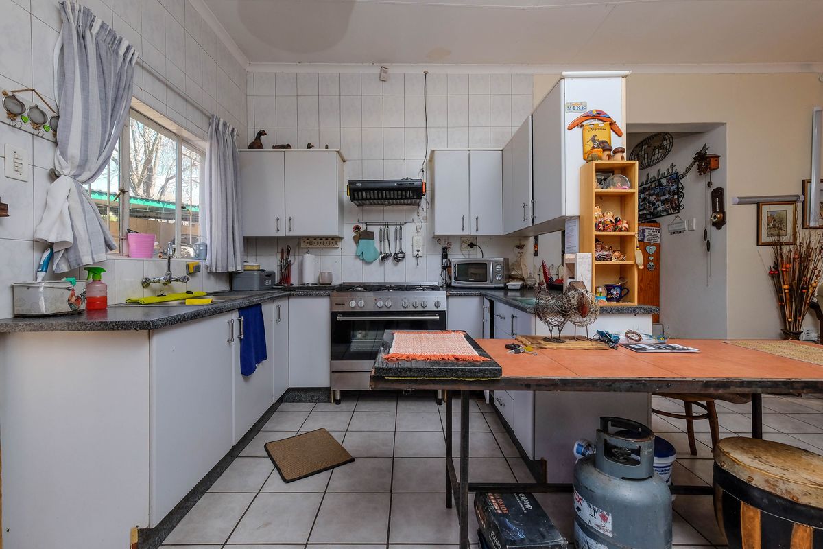 A functional kitchen featuring white cabinetry, laminate countertops, a gas stove with extractor fan, and tiled finishes throughout.