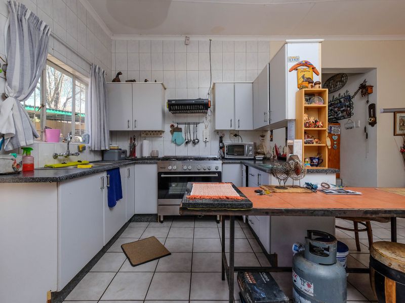 A functional kitchen featuring white cabinetry, laminate countertops, a gas stove with extractor fan, and tiled finishes throughout.