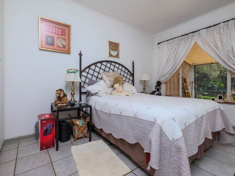 A bedroom featuring tiled flooring, a built-in cupboard, and a large window providing natural light and garden views.