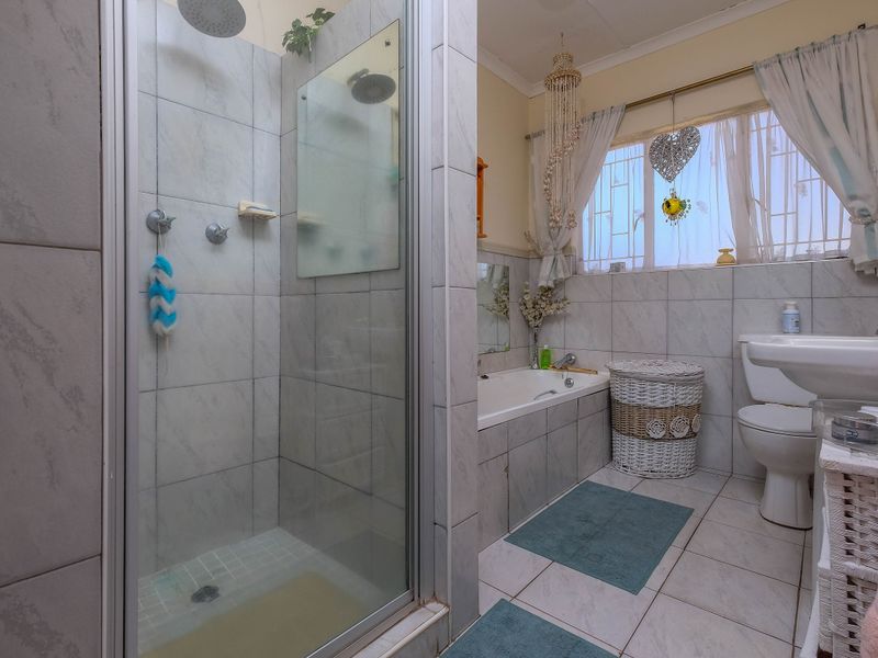 A functional bathroom featuring a separate shower enclosure, built-in bathtub, pedestal basin, and toilet with neutral ceramic tiling throughout.