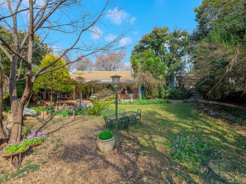 A spacious rear garden featuring mature trees, established landscaping, and a covered patio area attached to the main residence.