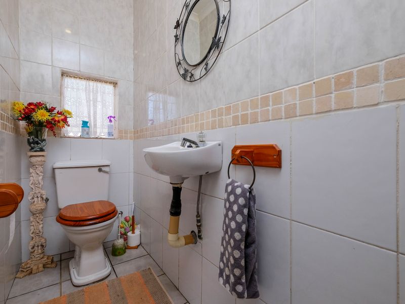 A compact bathroom featuring a wall-mounted basin, toilet, and full-height ceramic wall tiling.
