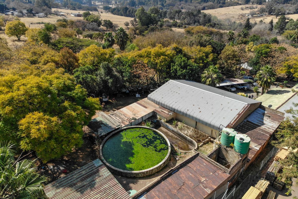 Aerial view of the property showing industrial-style structures, corrugated metal roofing, a large circular water reservoir, and external water storage tanks.