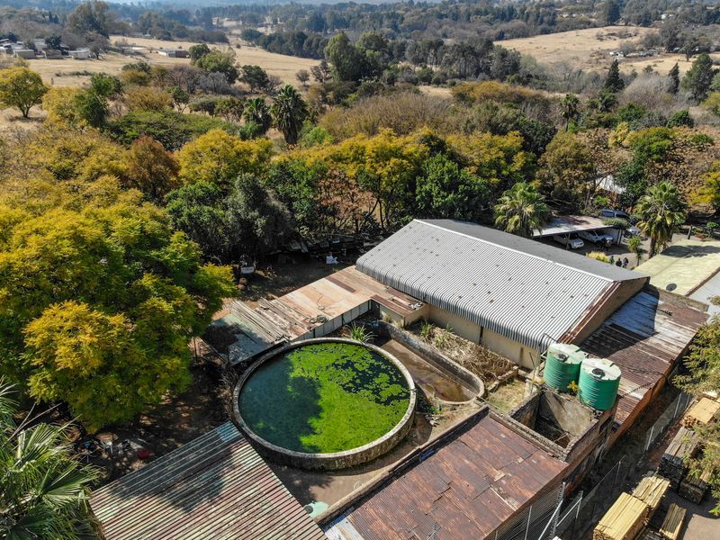 Aerial view of the property showing industrial-style structures, corrugated metal roofing, a large circular water reservoir, and external water storage tanks.