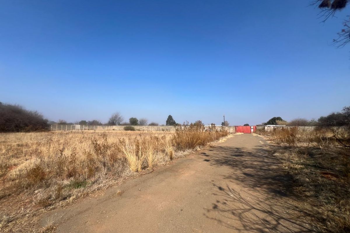 A view of a vacant residential plot featuring a paved driveway, perimeter walling, and a gated entrance.