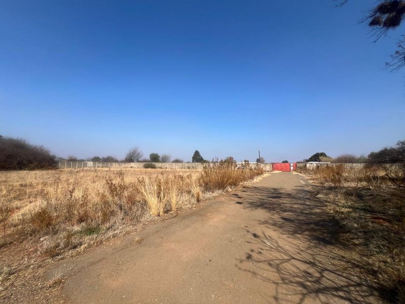 A view of a vacant residential plot featuring a paved driveway, perimeter walling, and a gated entrance.