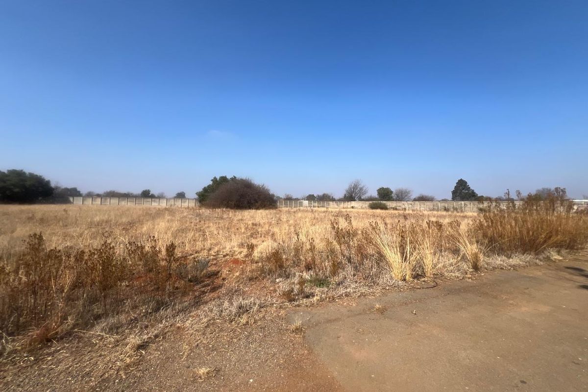 A vacant residential plot featuring dry grass and a perimeter wall, offering a clear space for future development.