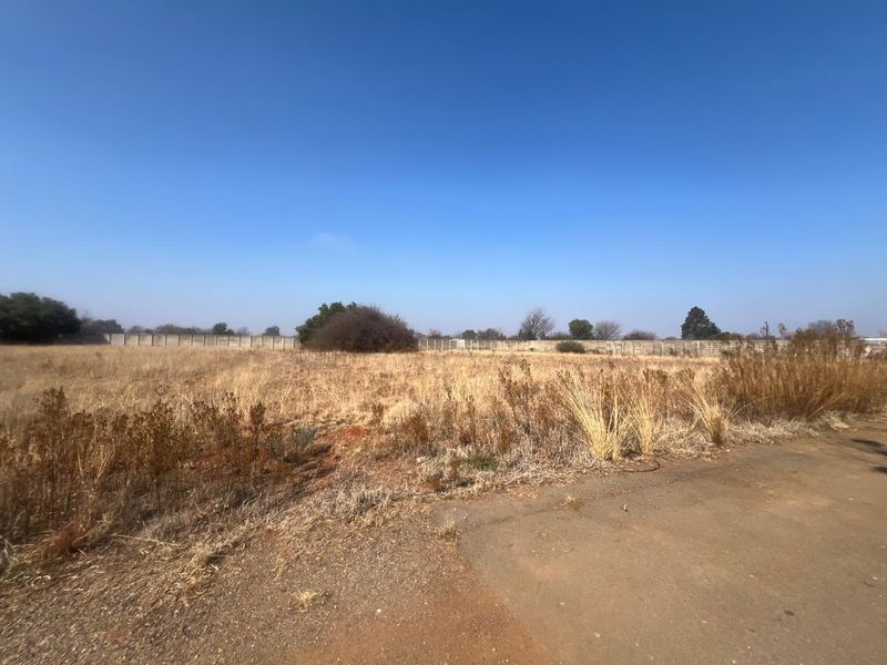 A vacant residential plot featuring dry grass and a perimeter wall, offering a clear space for future development.