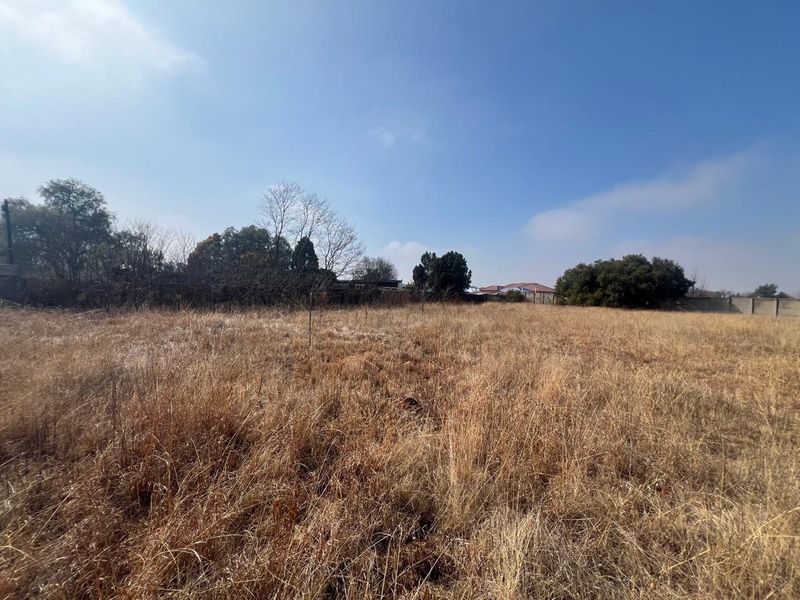 A wide-angle view of a vacant residential plot featuring dry grass and perimeter boundary walls, offering a blank canvas for future development.