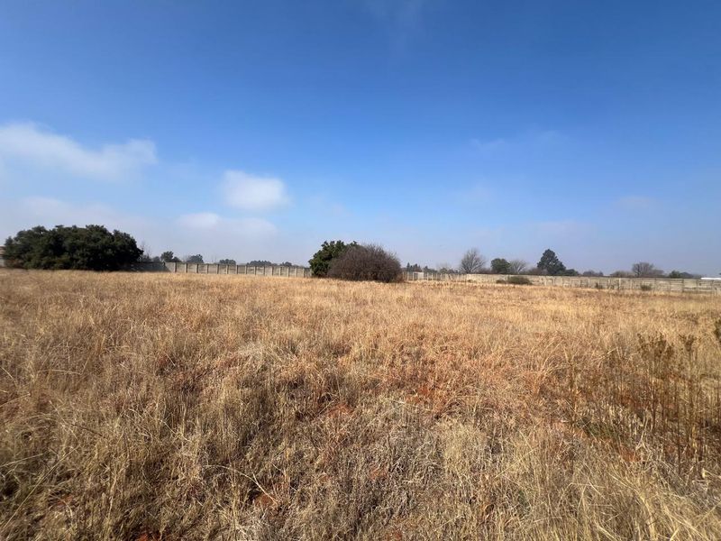 A vacant residential plot featuring dry grass and a precast concrete boundary wall along the perimeter.